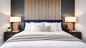 A modern bedroom with a bed, two bedside tables, a blue upholstered headboard, and a wall-mounted light fixture. - Empress Solace Villa (Friendswood)