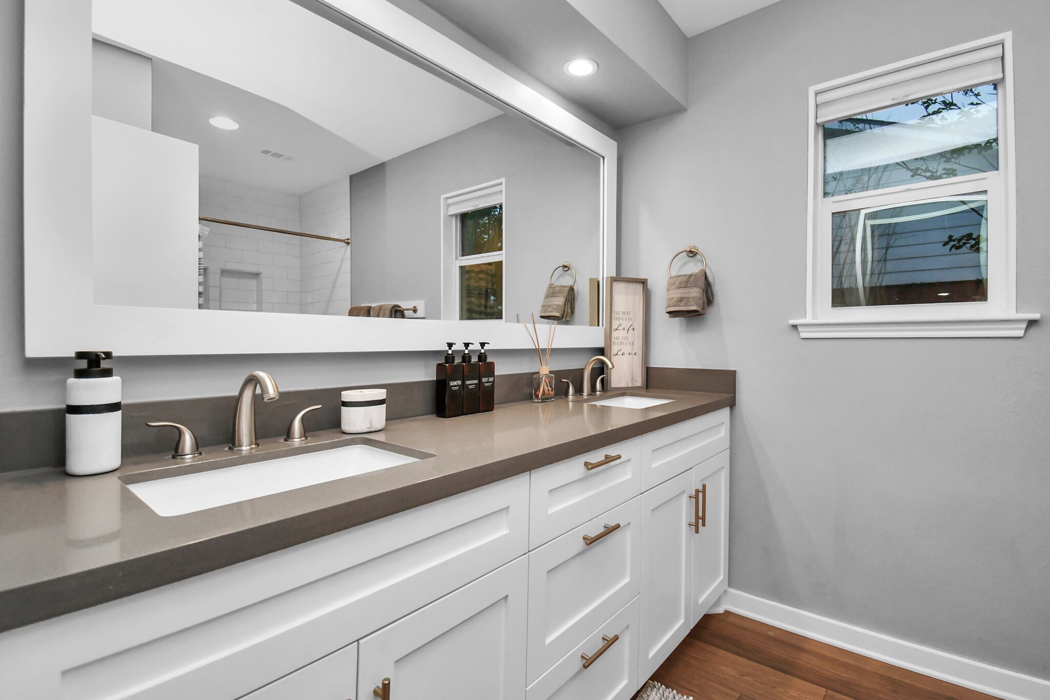 A bathroom with a large mirror, two sinks, and a window.