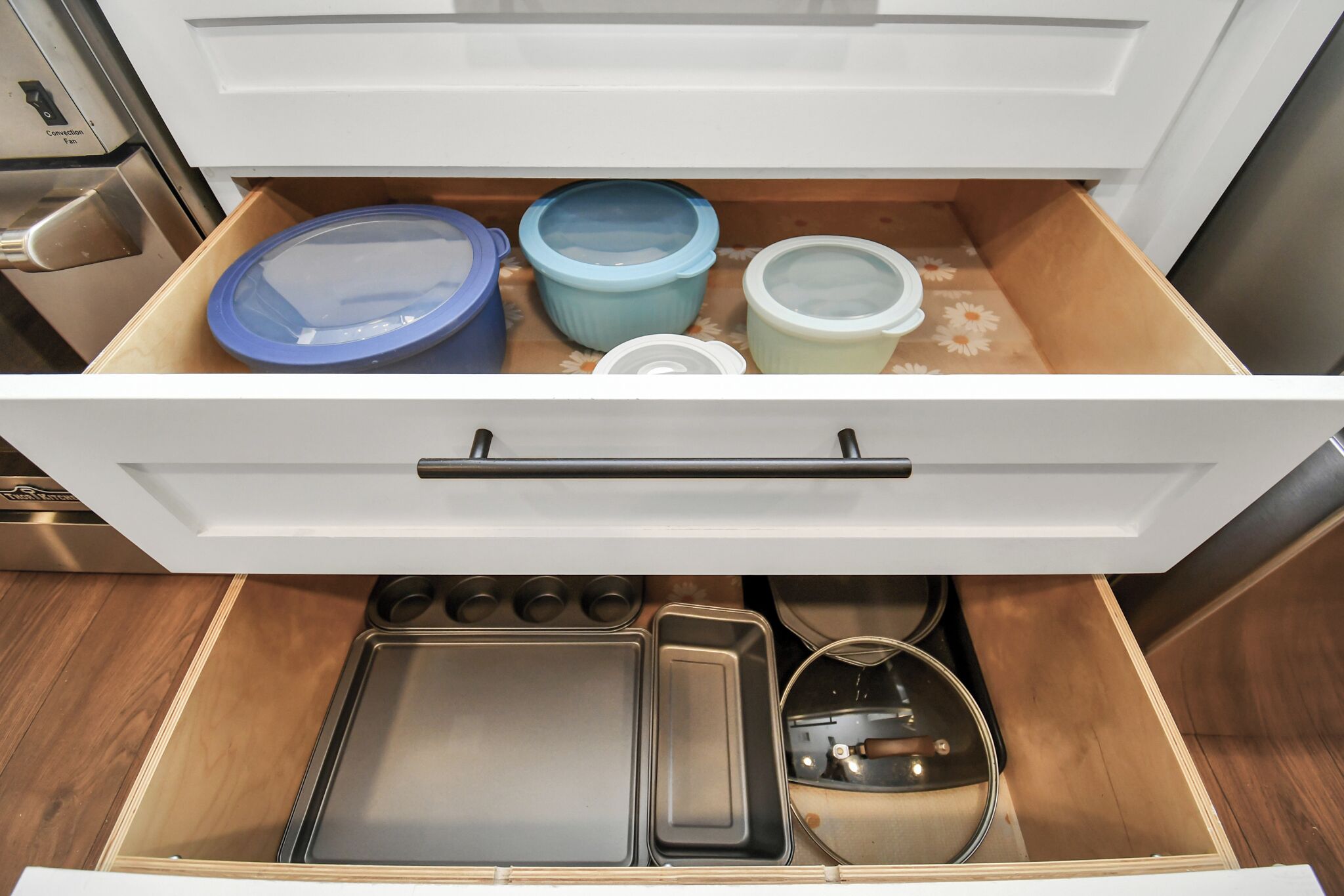 A kitchen drawer with storage containers, a baking tray, and a kettle.