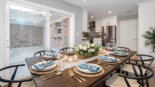 A dining area with a long table set for six, surrounded by chairs, with a kitchen in the background. - Empress Solace Villa (Friendswood)