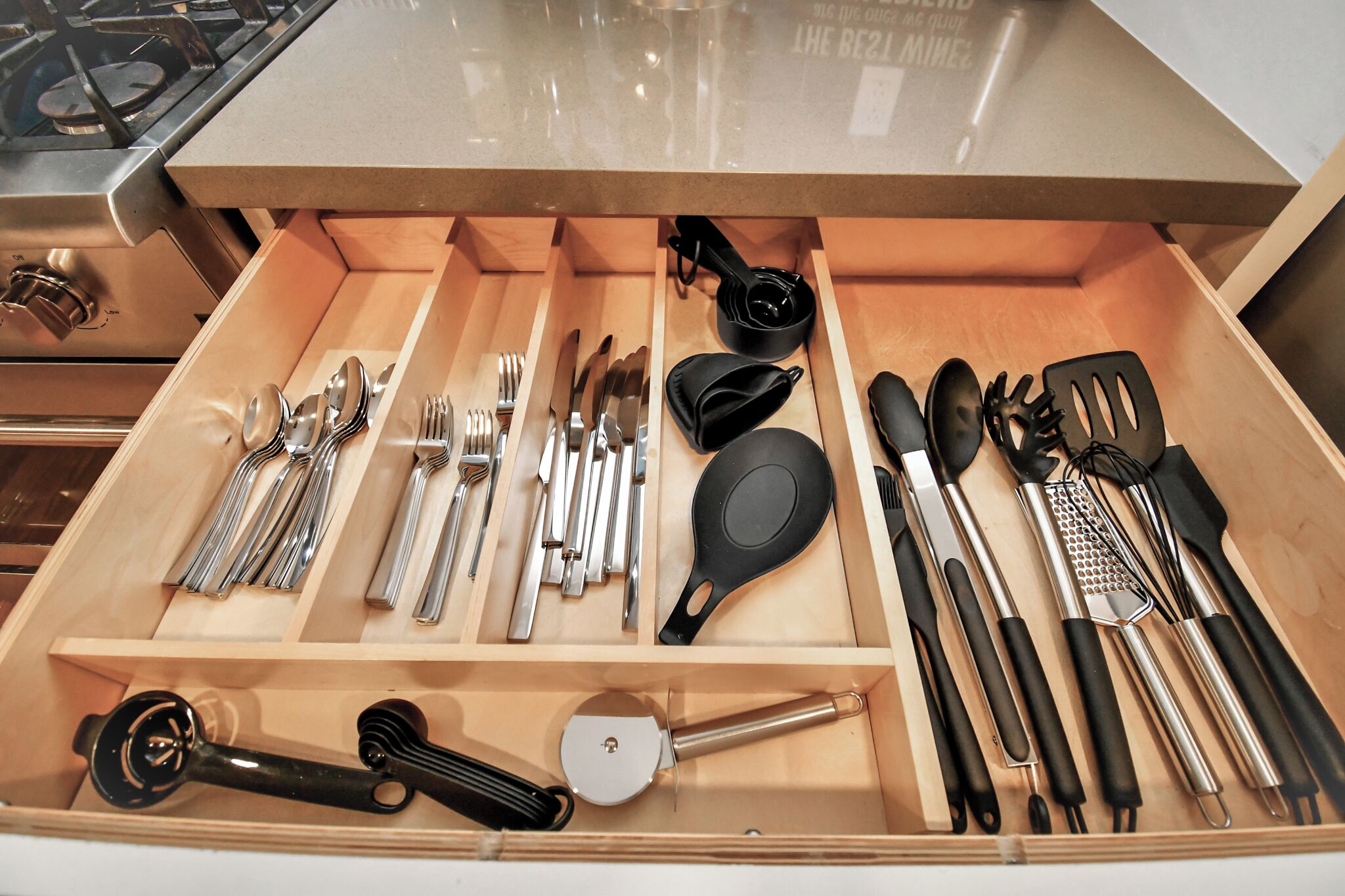 A drawer with various kitchen utensils including spoons, forks, knives, spatulas, and a grater.