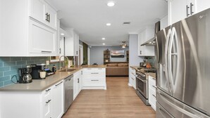 A modern kitchen with white cabinets, a stainless steel refrigerator, and a wooden countertop. - Empress Solace Villa (Friendswood)