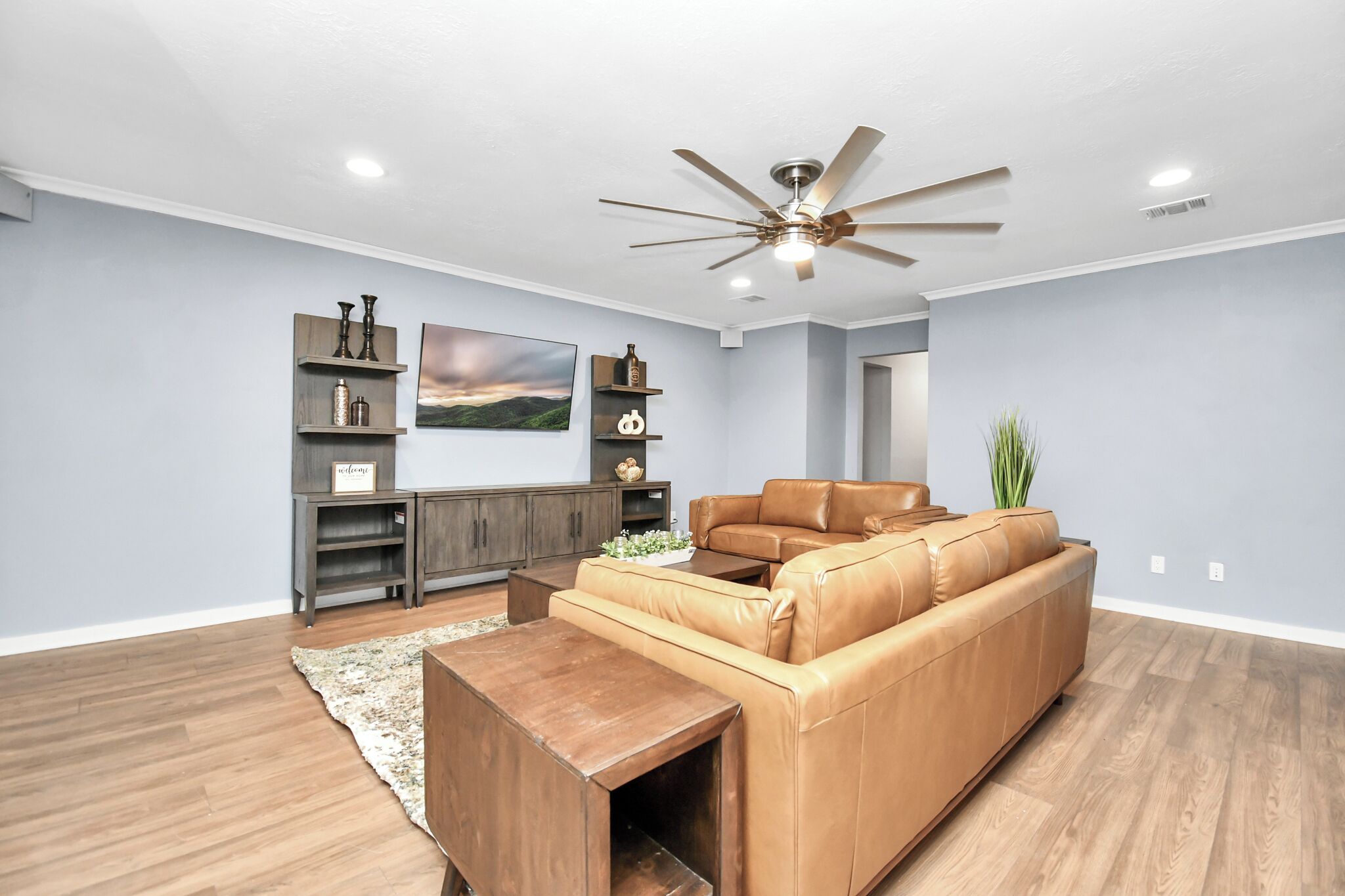 A spacious living room with a brown leather sofa, wooden coffee table, and a ceiling fan.