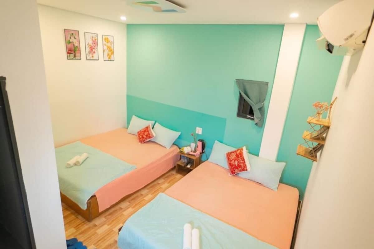 A room with two beds, a small table, and a wall-mounted shelf.