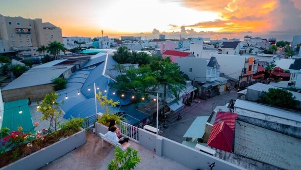 Una terraza en la azotea con mobiliario, vista panorámica de la ciudad y un atardecer.