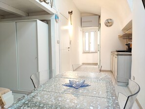 Un couloir étroit avec une table à manger au centre, bordé de placards et d’un coin cuisine.