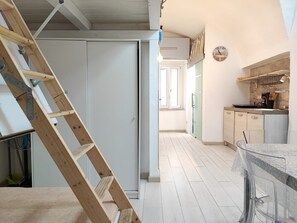 Une cuisine avec une échelle en bois, des placards, une fenêtre et une horloge au mur.