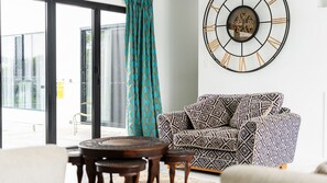 A modern living room with a patterned sofa, a round wooden table, and a large wall clock.