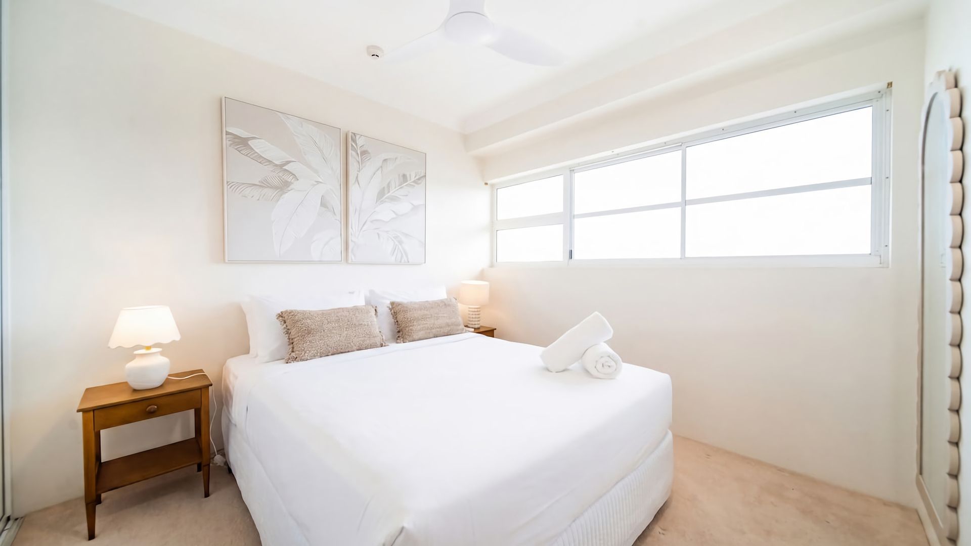 A bedroom with a large bed, two bedside tables, a ceiling fan, and a window with curtains.