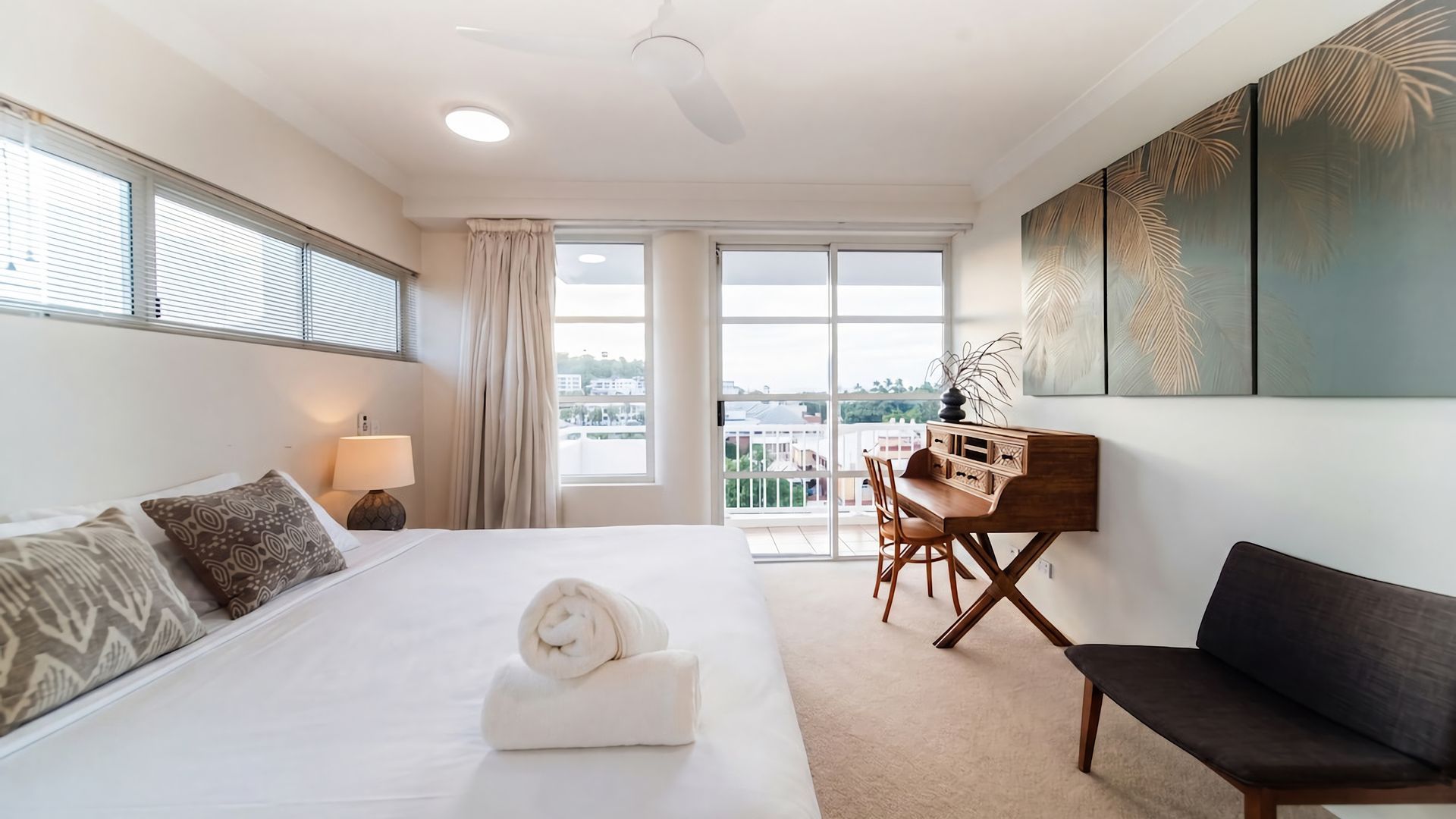 Habitación de hotel con cama, escritorio, silla, sofá y un amplio ventanal con vista a la ciudad.