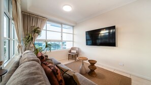 Un salon moderne avec un canapé, un fauteuil, un téléviseur à écran plat et une grande fenêtre.