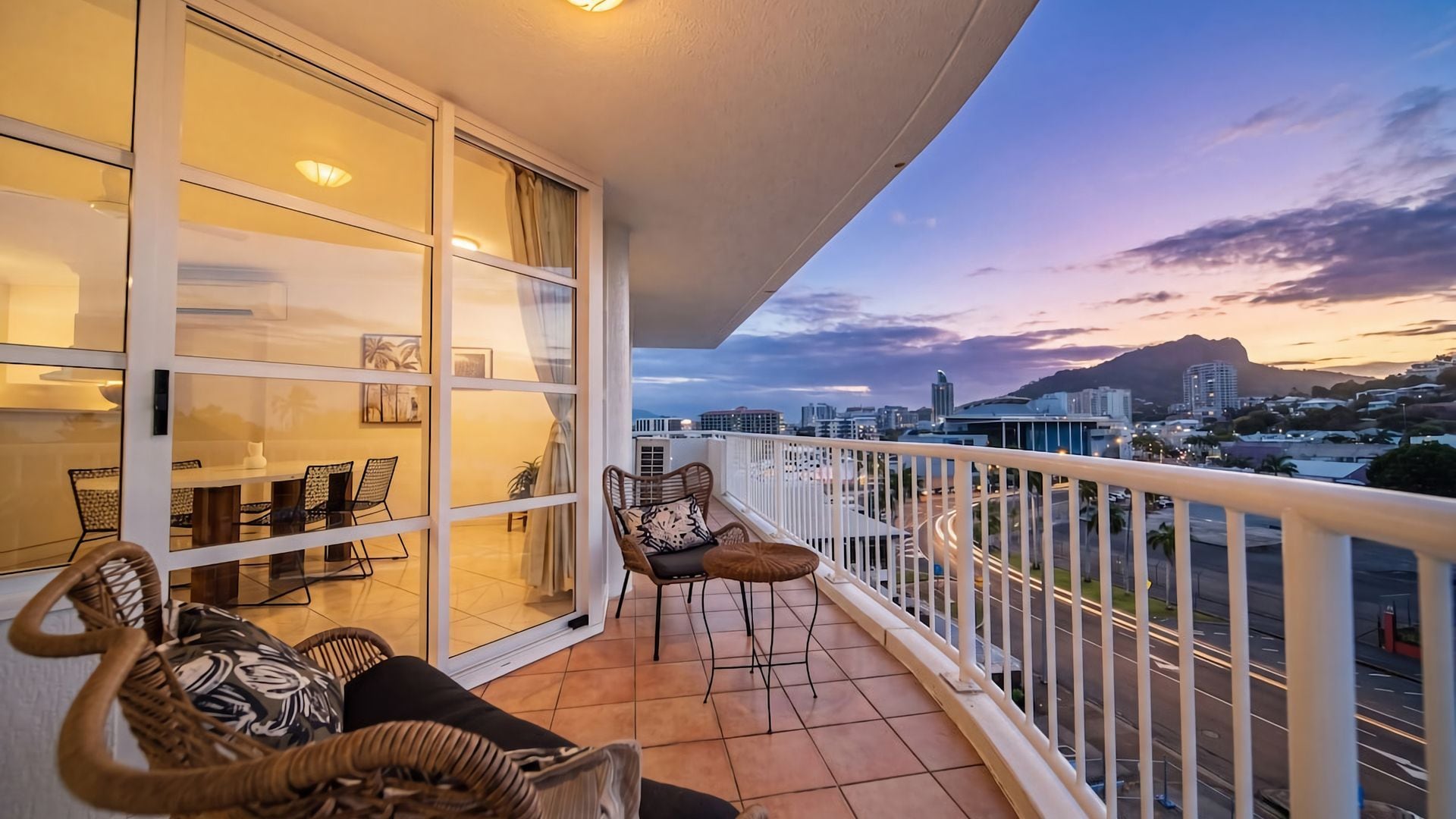 A balcony with a city view, a dining area with chairs and a table, and a large window with curtains.