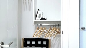 A room with a white door, a metal handle, a white wall, a black bench, and wooden hangers on a rack.