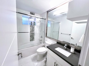 Un baño moderno con ducha envuelta en vidrio, inodoro blanco, encimera negra y un espejo grande.