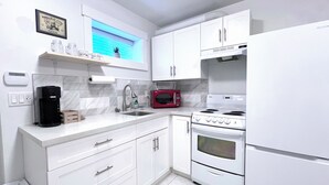 A modern kitchen with white cabinets, a stainless steel sink, a red microwave, a gas stove, and a coffee maker.