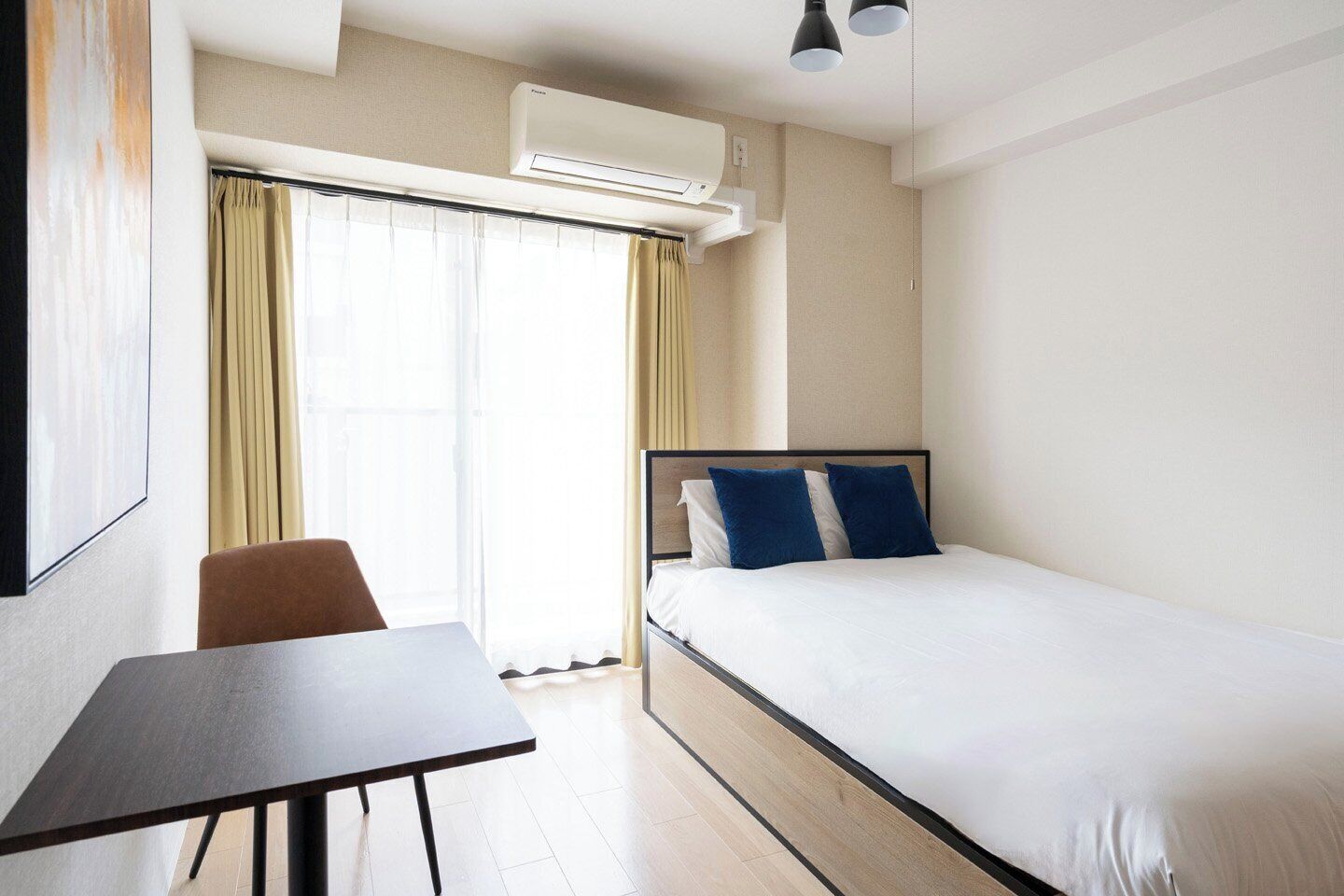 A hotel room with a bed, a desk, a chair, an air conditioning unit, and a window with curtains.