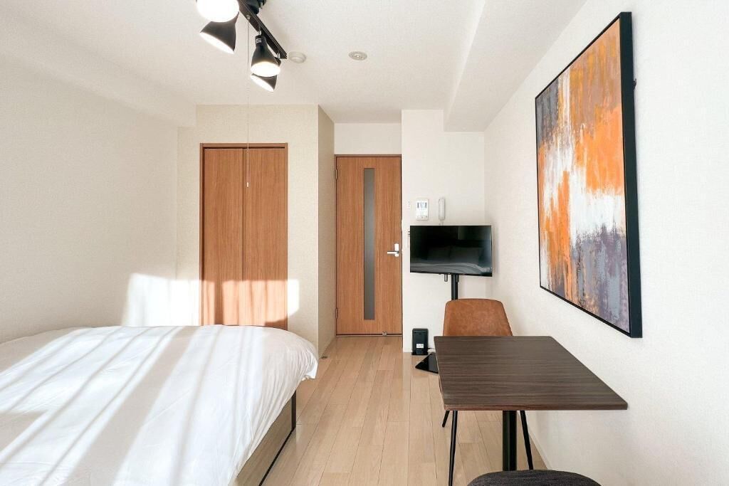 A hotel room with a bed, a desk, a TV, and a door.