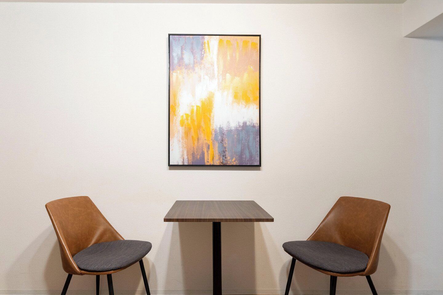 Quarto com duas cadeiras e uma mesa, um quadro na parede e uma parede branca lisa.
