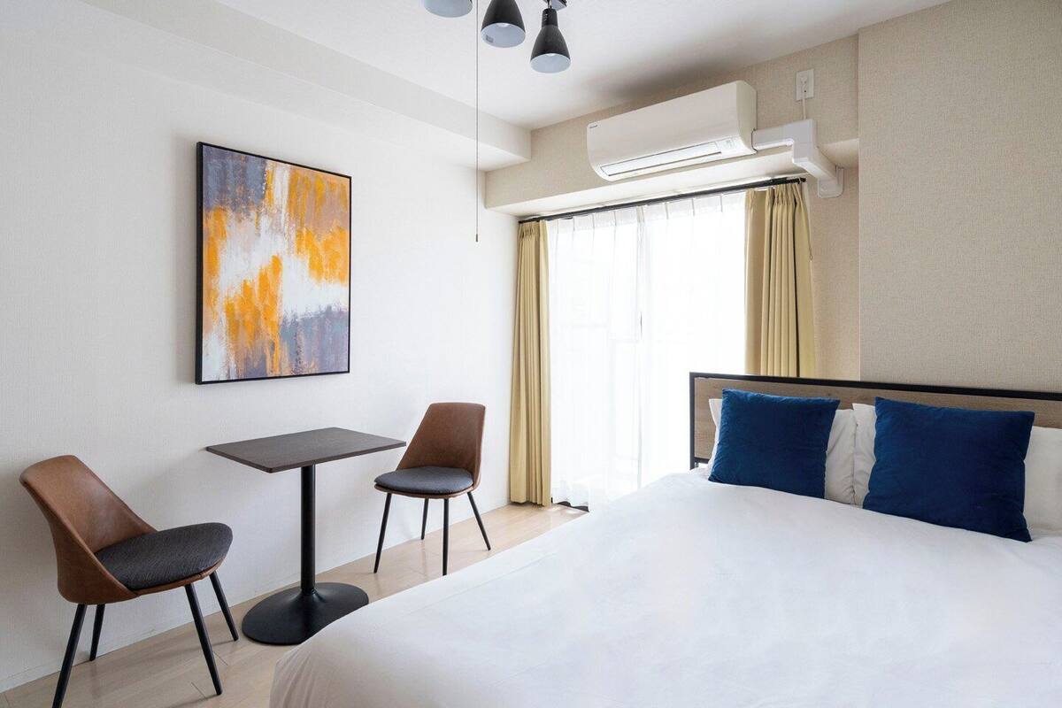 Habitación de hotel con cama, dos sillas, una mesita, aire acondicionado y ventana con cortinas.