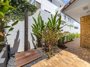 Ein moderner Außenbereich mit einer weißen Wand, einer Holzbank und einem kleinen Garten mit Pflanzen.