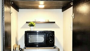 Una cucina compatta con un frigorifero in acciaio inossidabile, un forno a microonde sopra e un piccolo ripiano con una pianta e una tazza.