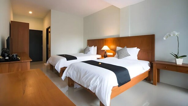 Habitación de hotel con dos camas, cabecero de madera, lámparas de noche, una mesita y una planta en maceta.
