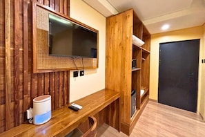 Una habitación con panel de madera, televisor montado, escritorio de madera, altavoz blanco y puerta negra.