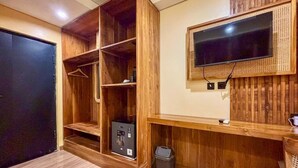 Una habitación con un armario de madera, un televisor instalado en un panel de madera y un cesto de basura pequeño.