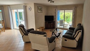 A living room with two sofas, a coffee table, a TV, and a sliding glass door leading to an outdoor area. - SEPTEMBER SPECIAL: Vacation Rental in St Gilles Croix de Vie (Le Fenouiller)