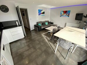 A modern living room with a sofa, a dining table, and a kitchen area with white cabinets. - Le Corbier lodge 43 2-bedroom apartment at the foot of the slopes (Villarembert)