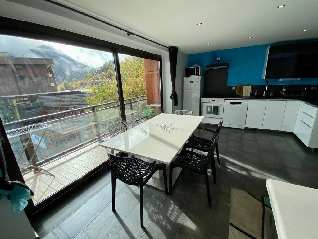 Une cuisine moderne avec des meubles blancs, une table à manger entourée de chaises noires et une grande fenêtre donnant sur un paysage montagneux.