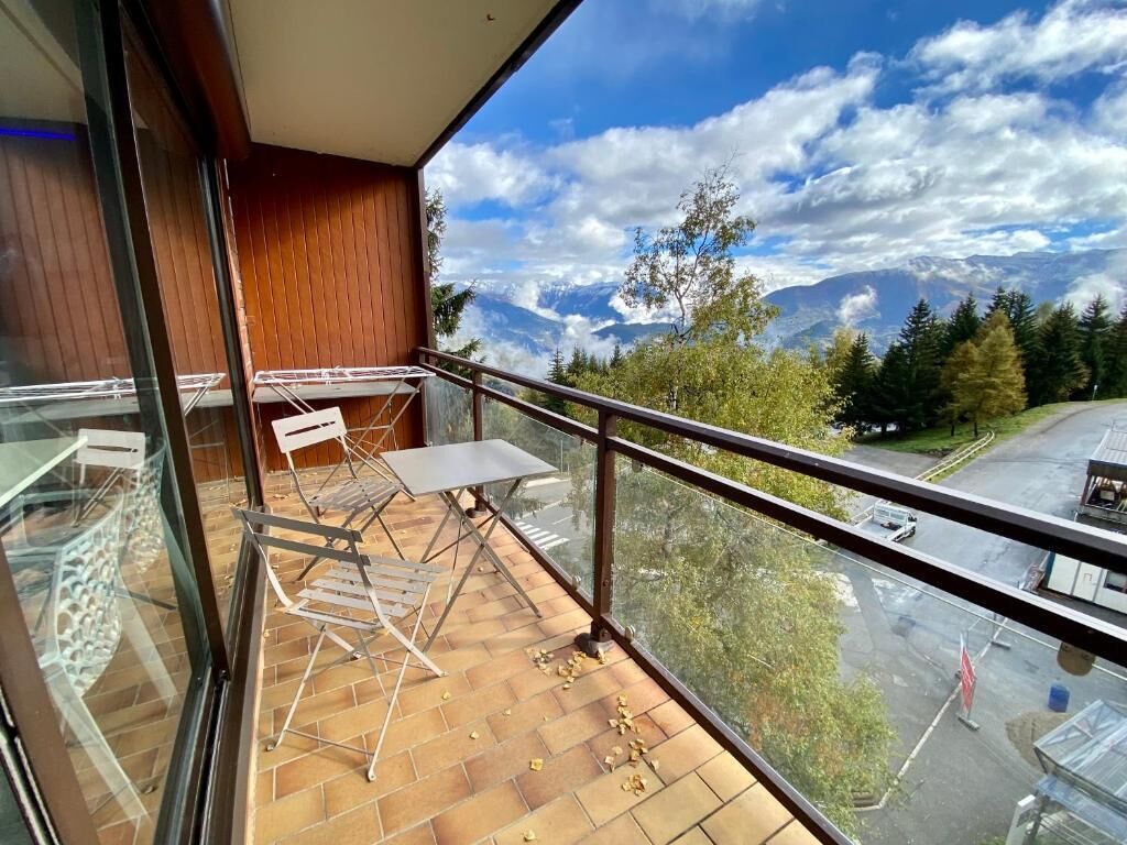 Ein Balkon mit Tisch und Stühlen, Blick auf Berge und ein Parkplatz.