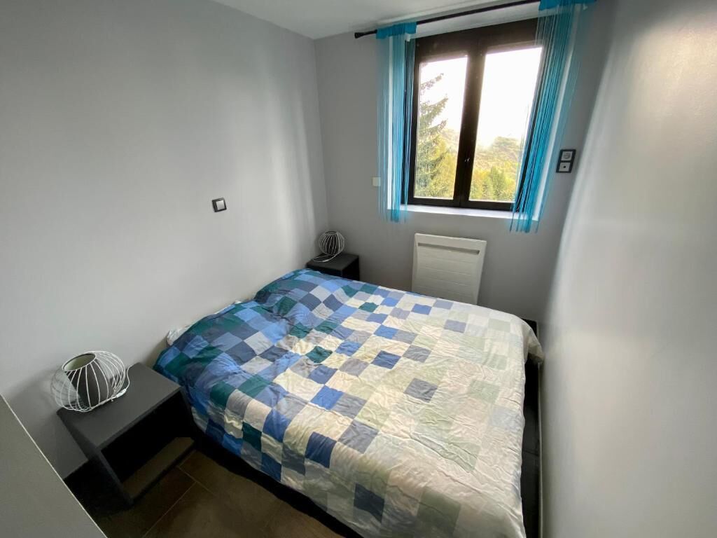 Een slaapkamer met een bed, nachtkastje, radiator en raam met gordijnen.