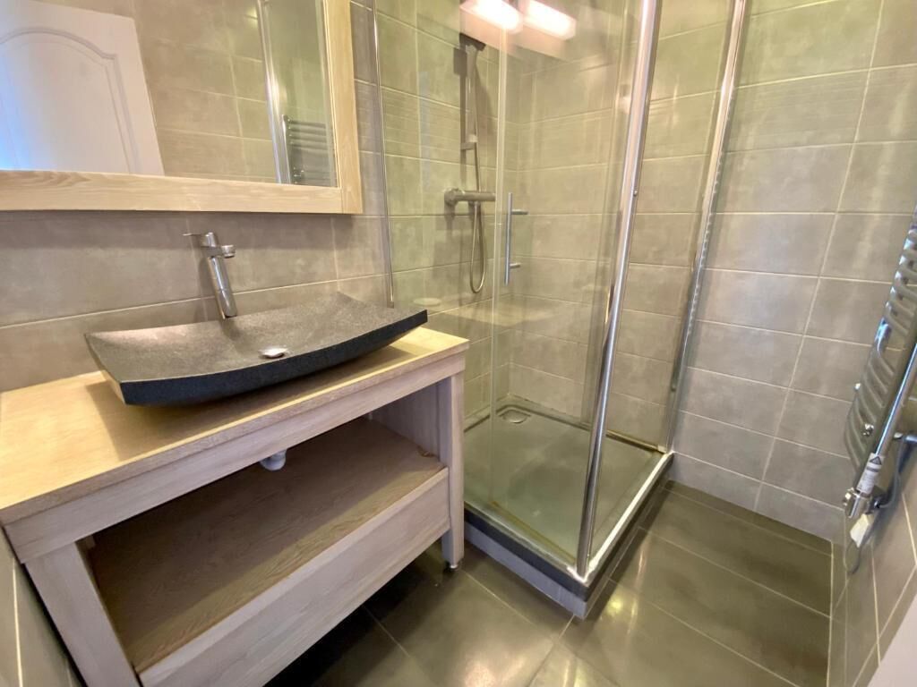 A bathroom with a glass shower enclosure, a sink with a dark countertop, and a mirror above the sink.