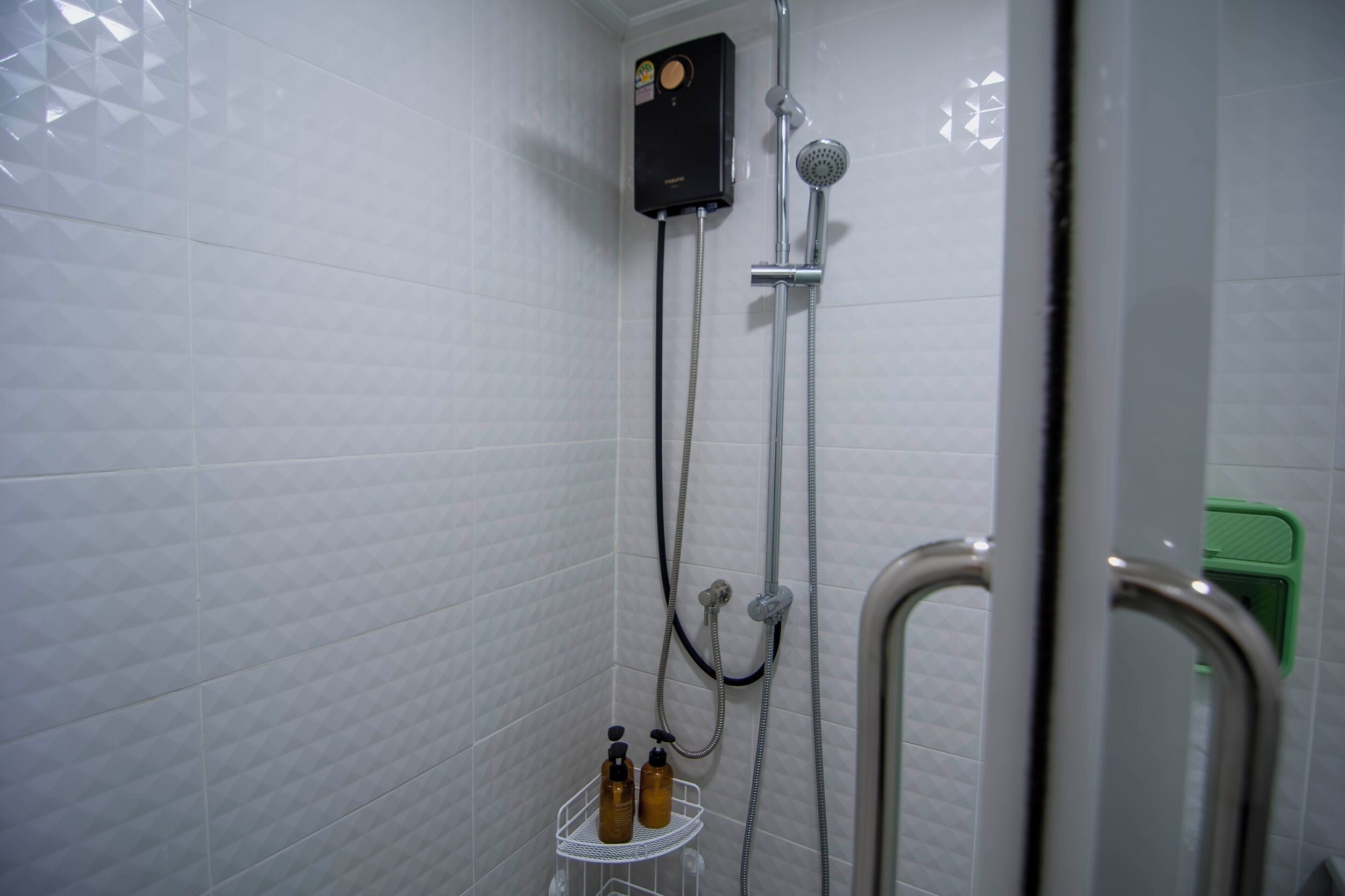 A shower with a control panel, a handheld showerhead, and a wall-mounted faucet.