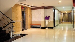A hotel lobby with a staircase, elevator, bench, and a vase with purple flowers. - Rosee Wood (Visakhapatnam)