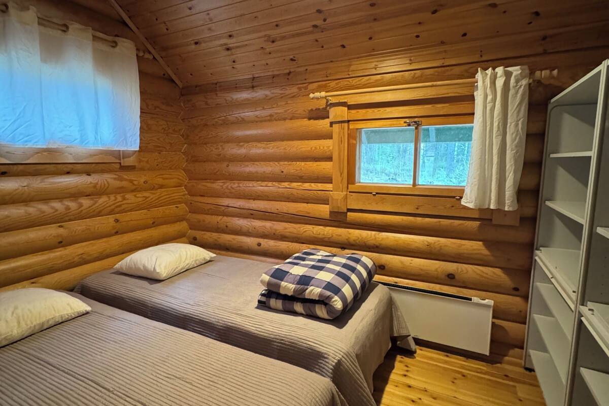 A log cabin room with two beds, a window with curtains, a radiator, and a white wardrobe.