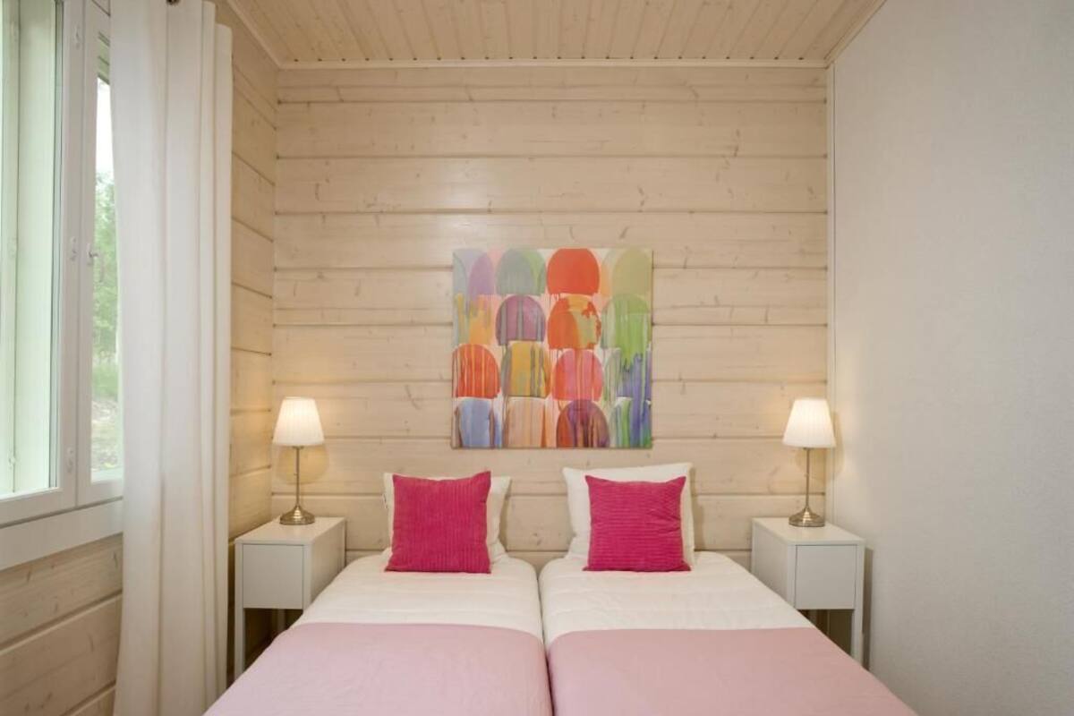 A double room with two beds, each with a pillow and a nightstand with a lamp.