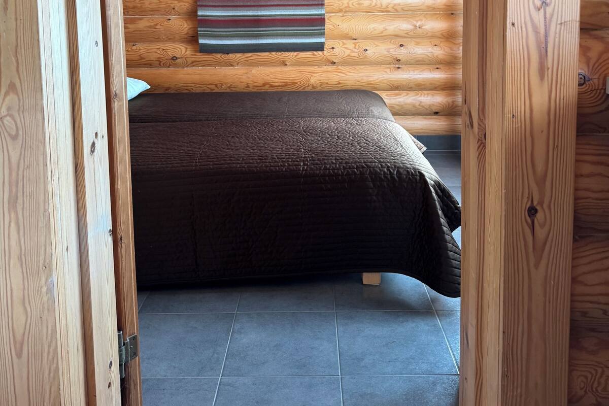 A wooden-paneled room with a bed, a striped wall hanging, and a tiled floor.