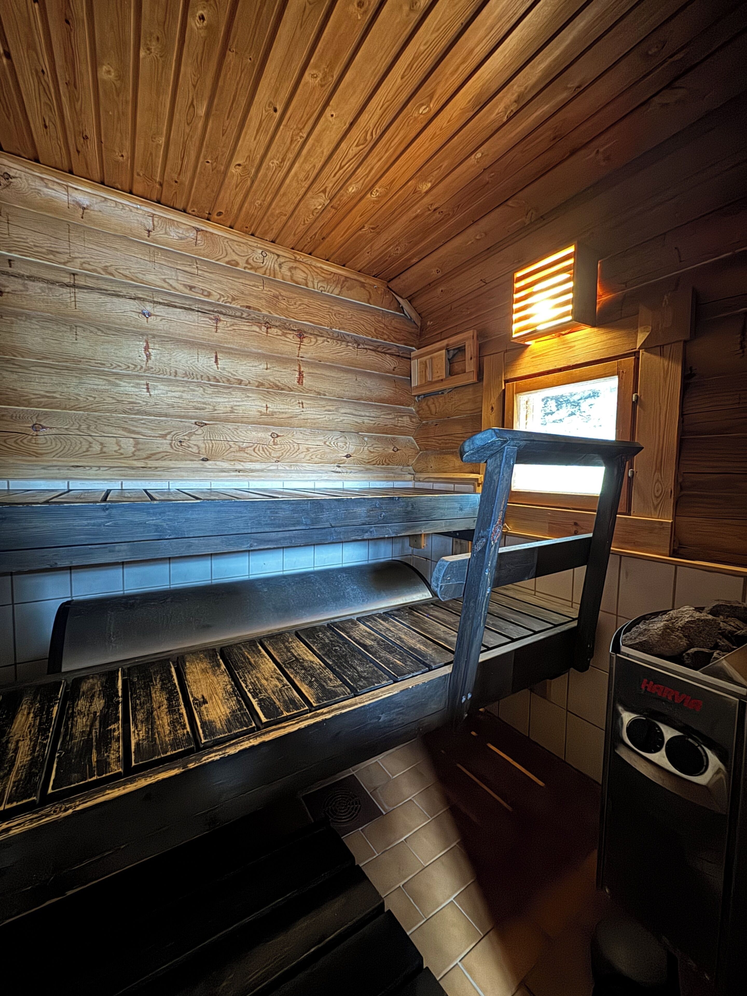 Interior de una cabaña de madera con un banco, una ventana y una estufa.
