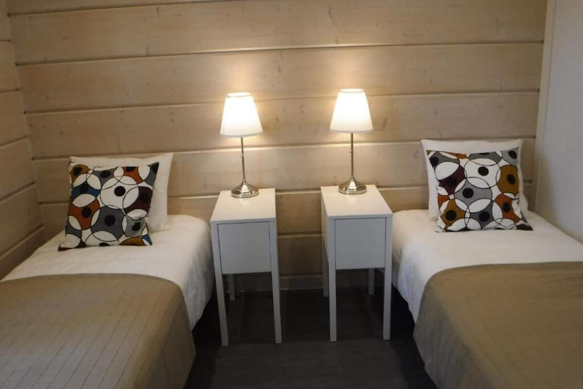 A hotel room with two beds, each with a patterned pillow, two bedside lamps, and a wooden headboard.