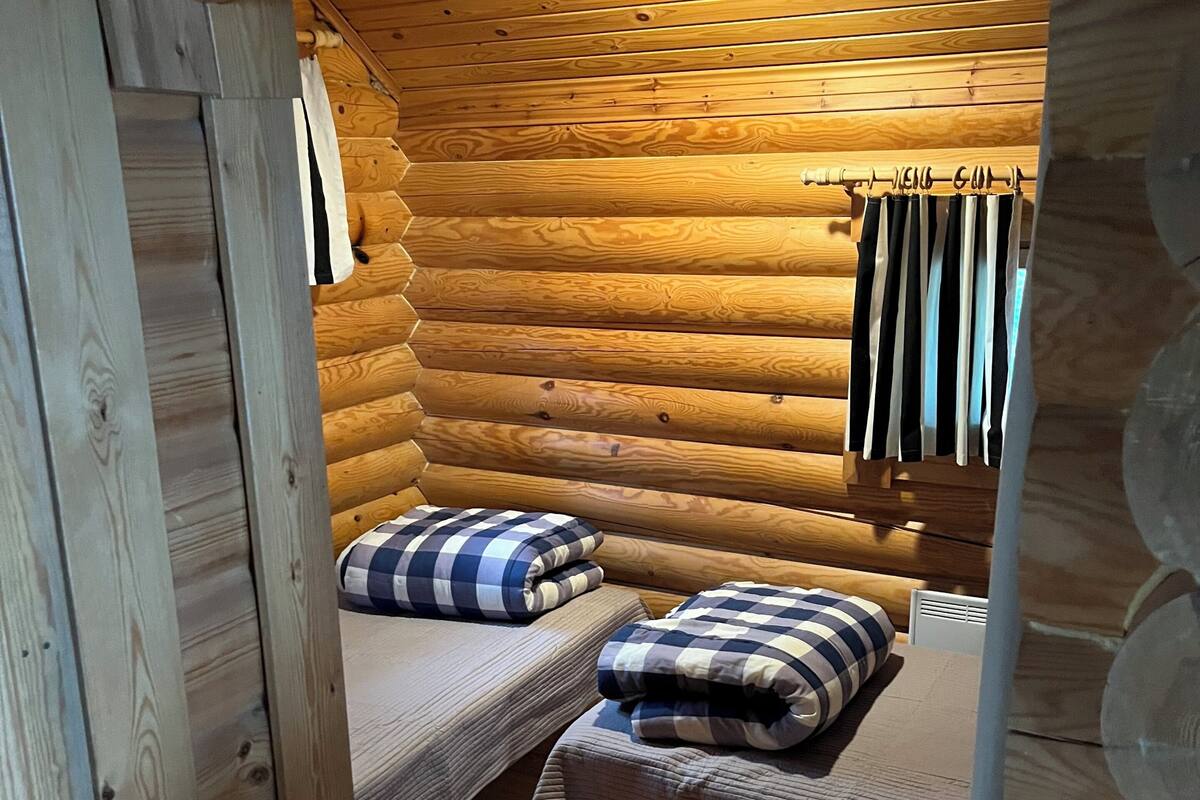 A log cabin room with two beds, a wooden ceiling, and a hanging rack with towels.