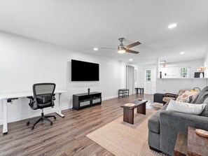 Ein modernes Wohnzimmer mit Flachbildfernseher, Deckenventilator, grauem Sofa, Couchtisch und Schreibtisch mit Stuhl.