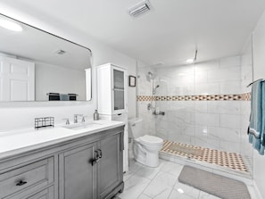 Et moderne badeværelse med vaskemøbel, toilet, brusebad og flisegulv.