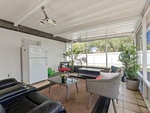 Ein Wohnzimmer mit einer Couch, einem Sessel, einem kleinen Tisch, einem Kühlschrank und einem großen Fenster.