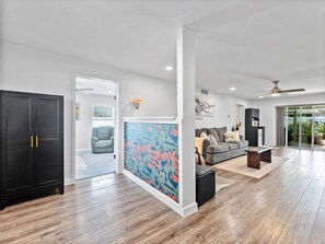 Ein großzügiger Wohnbereich mit einem großen schwarzen Kleiderschrank, einem farbenfrohen abstrakten Gemälde, einem grauen Sofa und einem Deckenventilator.