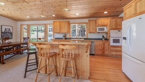 Een keuken met houten kastjes, een centraal eiland met krukken, een magnetron en een koelkast.