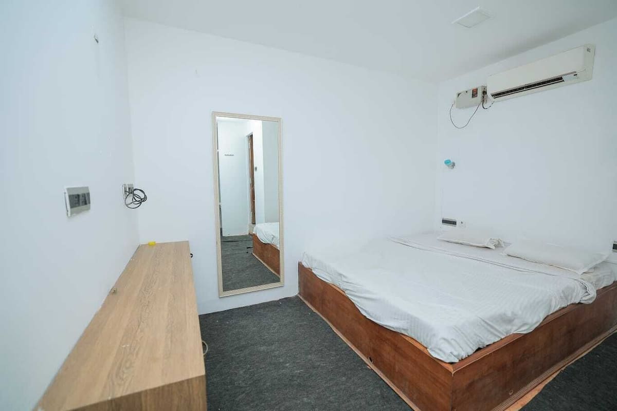 Un dormitorio con una cama de madera, un espejo, una mesita de noche y un equipo de aire acondicionado.