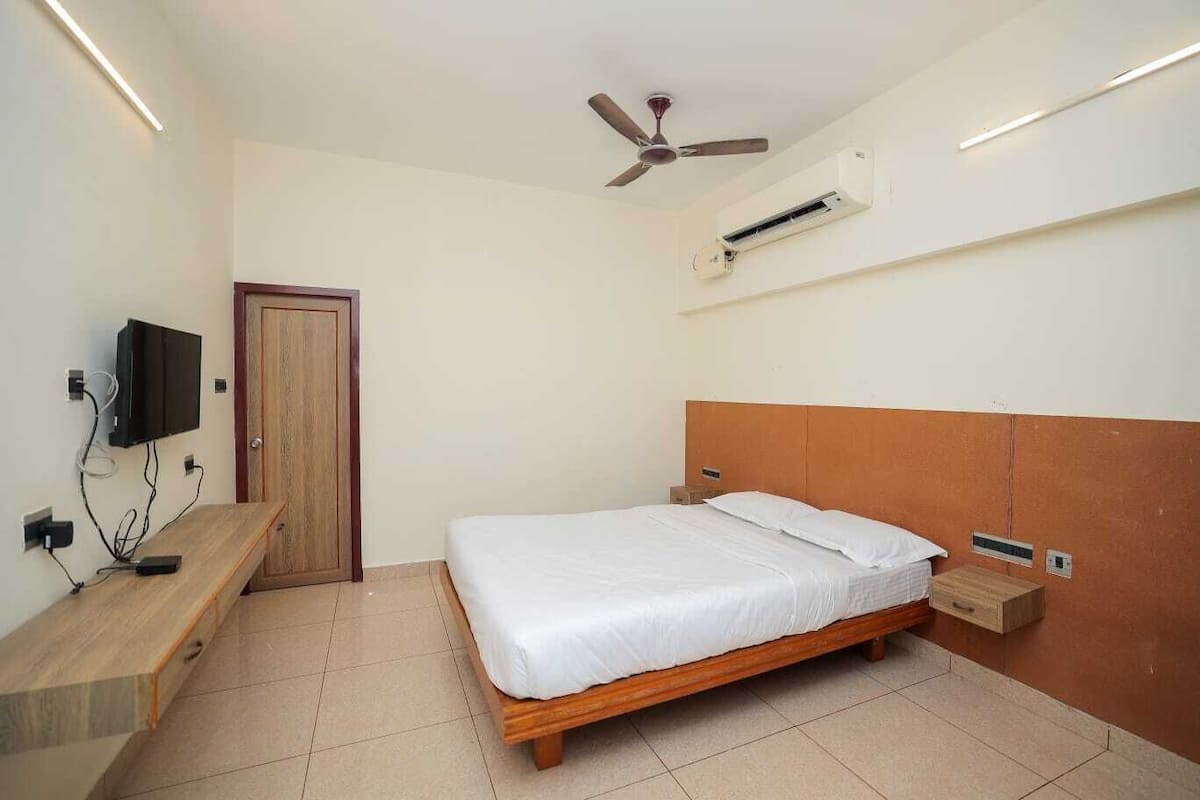 Un dormitorio con cama, ventilador de techo, unidad de aire acondicionado, televisor y banca de madera.