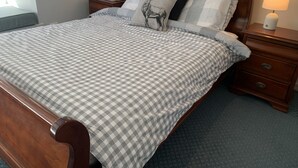 A neatly made bed with a checkered bedspread, two bedside tables with lamps, and a decorative pillow with a deer image. - Glacier Chalet (Dinner Plain)